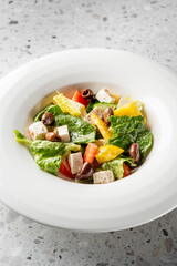  A fresh and vibrant salad featuring romaine lettuce, yellow bell peppers, tomatoes, black olives, and feta cheese, served in a white bowl on a textured surface.