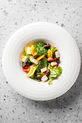  A fresh and vibrant salad featuring romaine lettuce, yellow bell peppers, tomatoes, black olives, and feta cheese, served in a white bowl on a textured surface.