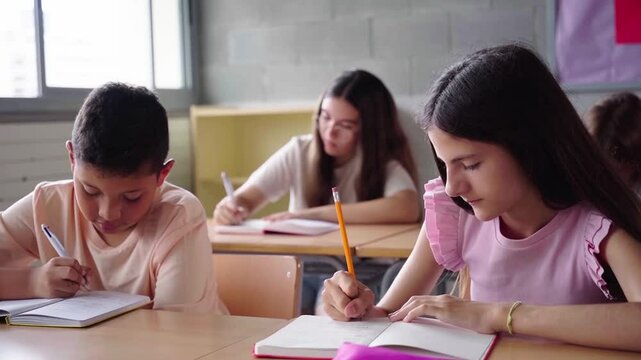 View of a group of preteens in primary school concentrated studying in the classroom doing homework writing on a notebook. Copy space footage.