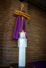 A candle lit with a cross draped in purple for observance of Lent in the background