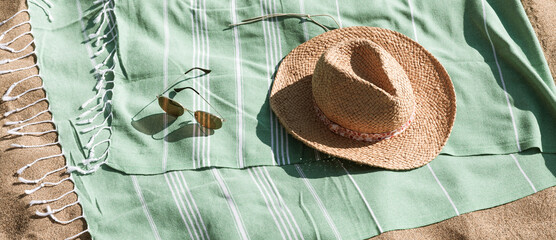 Green towel, straw hat, sunglasses on beach sand background. Aesthetic lifestyle, summer vacation concept. Sunbathing, beach party, holiday picnic. Travel fashionable blog, social media, top view.