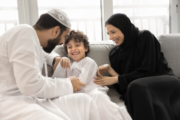 Happy Arabian family dressed in traditional Muslim attire enjoy active playtime at home. Young...