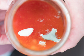 A hand holds a jar of tomato sauce with mold, indicating spoilage and storage errors