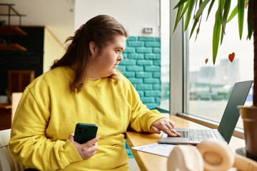 Young woman with Down syndrome enjoys cozy cafe atmosphere while working on her laptop