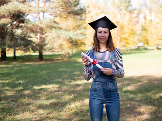 A joyful young woman wearing a graduation cap holds her diploma proudly outdoors amidst colorful...