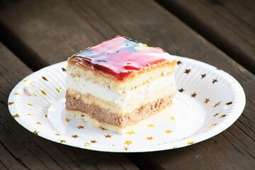 A slice of cake with red candy on top, two tiers: one with milk chocolate and the other with cream. On a white birthday plate with gold stars. Birthday party.