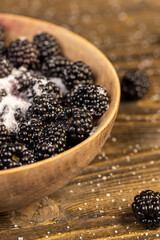 ripe black blackberries in a wooden bowl sprinkled with sugar