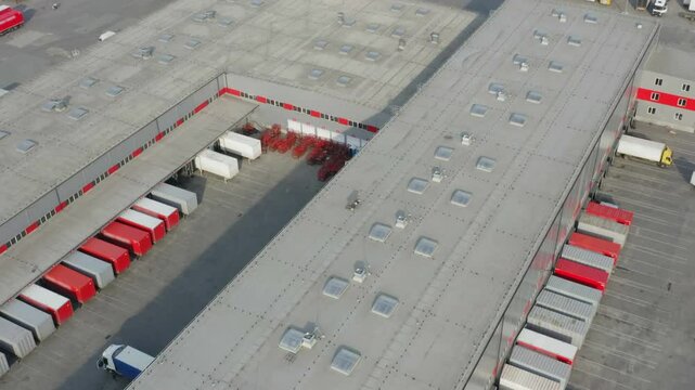 Modern logistics warehouse with trailers at loading ramps, drone aerial shot, state-of-the-art sorting hub in daylight