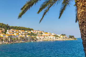 Obraz premium Korcula town in island of Korcula in Adriatic sea in Croatia, Europe. Coastal town with orange rooftops, tranquil blue sea, framed by palm fronds on a sunny day, offering a serene Mediterranean vista.