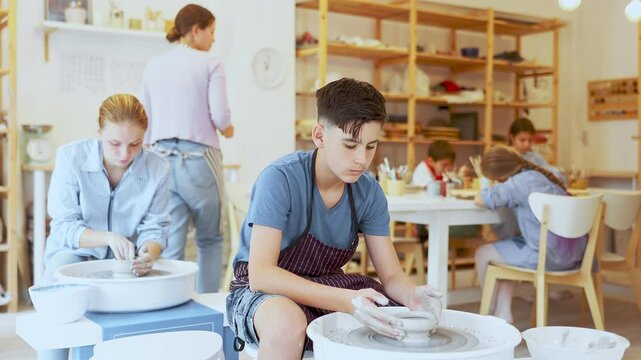 Pleased underage attendees of pottery circle working at throwing-wheel with female instructor