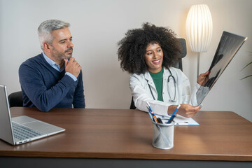 Beautiful female african doctor and mature latin patient looking at x-ray or MRI concept...