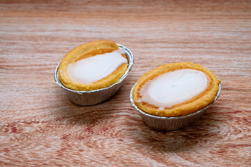 Two mazarin tarts sit on a wooden surface, showcasing their crispy golden edges and creamy white...