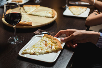 Hands taking slices of four-cheese pizza at a table