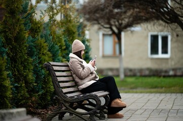 Fototapeta premium Person enjoying a quiet moment on a park bench while engaging with a mobile device amidst lush greenery and cozy surroundings