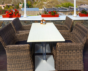 Outdoor restaurant, Wicker chairs and tables set for service. Potted flowers decorate the space.