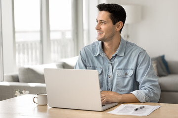 Young man sit at desk with laptop, looking away, engaged in remote work or creative tasks completion, smile, feel satisfied with work result, think about new professional achievements or opportunities