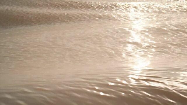 Waves gracefully roll towards the sandy beach as the sun sets on the horizon, casting a warm glow across the water. The peaceful atmosphere invites relaxation and reflection