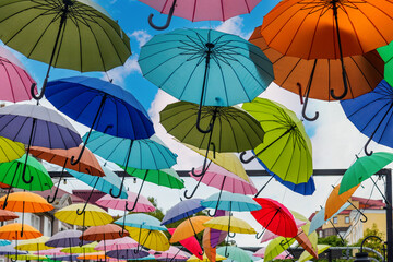 On the background of blue sky with light clouds bright umbrellas of different colors are seen, creating contrast and good mood.
