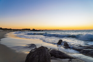 La plage des Amiets s&rsquo;embrase sous un ciel orang&eacute; et dor&eacute;. Les vagues laissent des reflets scintillants sur le sable mouill&eacute;, tandis que les rochers se d&eacute;coupent dans cette lumi&egrave;re cr&eacute;pusculaire.
