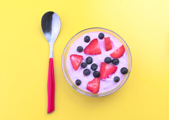 Fresh yogurt with berries in a bowl on a yellow background