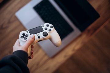 Gaming Controller Held Above Laptop on Wooden Surface