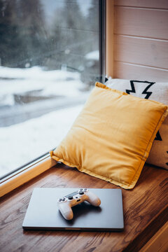 Cozy gaming nook with laptop, controller, and pillow by window
