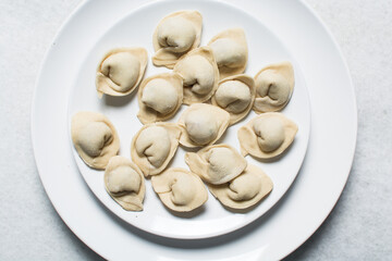 Overhead view of raw homemade wontons on a white plate, top view of chicken dumplings on white background, process of making dumplings