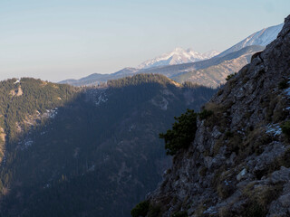 Striking Rocky Mountain Ridge Against Clear Sky with Distant Snow-Covered Peaks in Morning Light