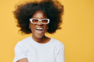 Smiling African woman with curly hair, wearing glasses and a white shirt, vibrant yellow background exuding joy and positivity