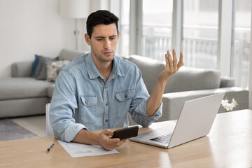 Young businessman looks at calculator with puzzled, disappointed expression, experiences issues in...