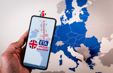 Hand holding smartphone displaying ETA or Electronic Travel Authorization over a map of europe