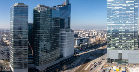 Modern skyscrapers with glass facades in Warsaw, Poland, surrounded by roads, smaller buildings,...
