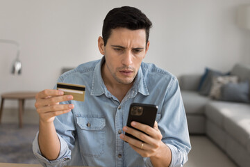 Man stare at phone screen while hold card, getting problems with online bank account, insufficient...