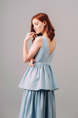 Sensual studio portrait of ginger woman in blue evening dress. Natural make-up and curly hairstyle. Summer feminine look, bridesmaid's fashion, outlook for hen party. Sleeveless gown with tiered skirt
