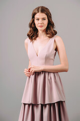 Romantic brunette woman in dust pink dress. Modern bridesmaid's summer fashion. Powder plunge neck sleeveless maxi gown with tiered skirt, sexy top. Trendy outlook for hen party, studio portrait