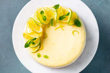 Lemon cheesecake with fresh lemon, lime and mint on a white plate. Grey background. Close up. Top...