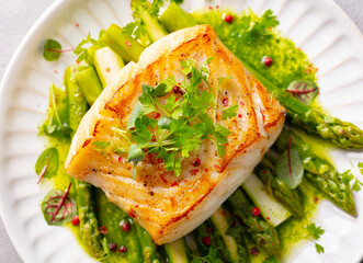 Fried cod with asparagus and on plate. Grey background. Close up. Top view.