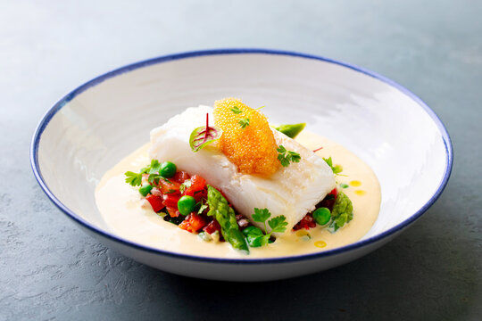 Roasted halibut fish with vegetables and pike caviar. Grey background. Close up.