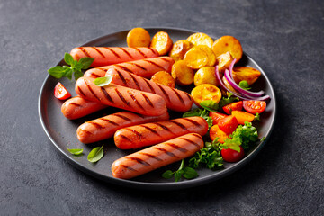 Sausages with roasted cherry tomatoes, potatoes and onion on a plate. Dark background. Close up.