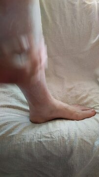 Un primer plano de una una mujer coloc&aacute;ndose crema para hidratar la piel de la pierna y pie, en su hogar. Video Vertical.