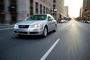 Silver sedan driving through an urban cityscape at dusk