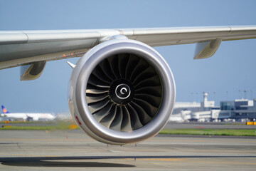 Close-up of jet engine turbine at airport runway with terminal in background