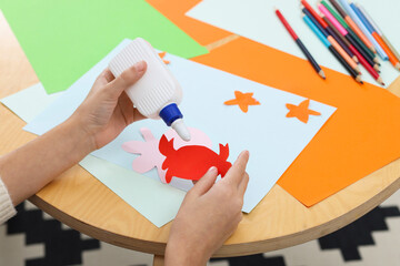 Girl applying glue onto paper figure for her creative project at table indoors, closeup. Art and...
