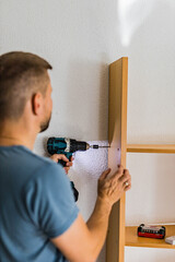 Young man assembling wooden shelf with electric drill while DIY and home renovation.Do It Yourself