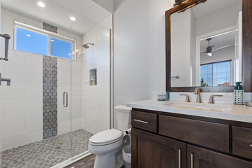 A modern bathroom with a toilet, sink, mirror, and walkin shower