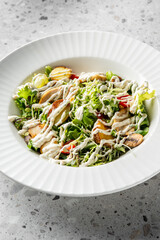 A fresh salad featuring mixed greens, sliced chicken, and a drizzle of creamy dressing, served in a decorative white bowl on a textured gray background.