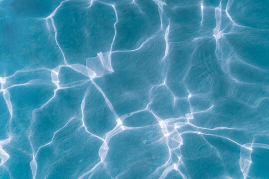 Background of transparent blue sea water glares under the rays of the sun. Sun glare at the bottom of the sea. Top view.