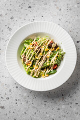 A fresh salad with leafy greens, cherry tomatoes, corn, and drizzled dressing, served in a white bowl on a textured surface. Perfect for healthy eating.