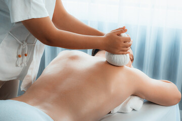 Hot herbal ball spa massage body treatment, masseur gently compresses herb bag on man body....