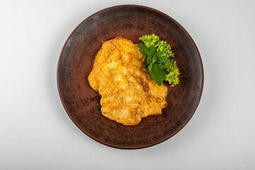 Golden crispy chicken schnitzel on a rustic clay plate, garnished with fresh parsley and lettuce. Traditional European cuisine, homemade comfort food, and delicious fried cutlet
